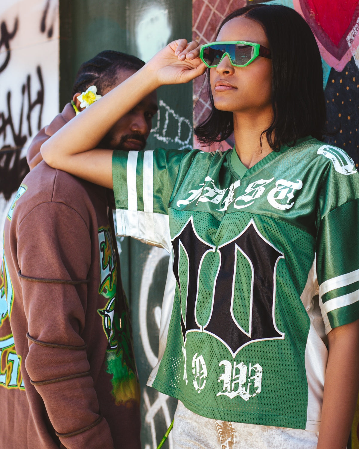Woman in a green mesh football jersey and green sunglasses by a graffiti wall