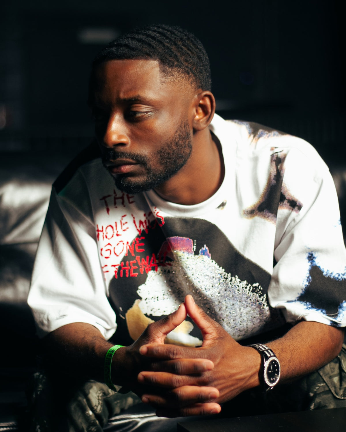 Man in a white graphic tee sitting with his hands folded